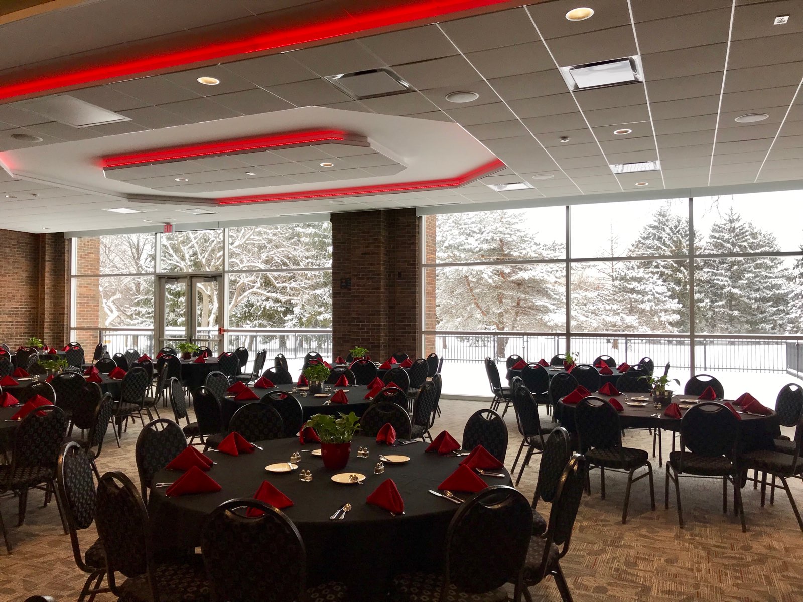 Ballroom set with black-draped round tables, a small stage, brick walls, and red accent lighting overhead.