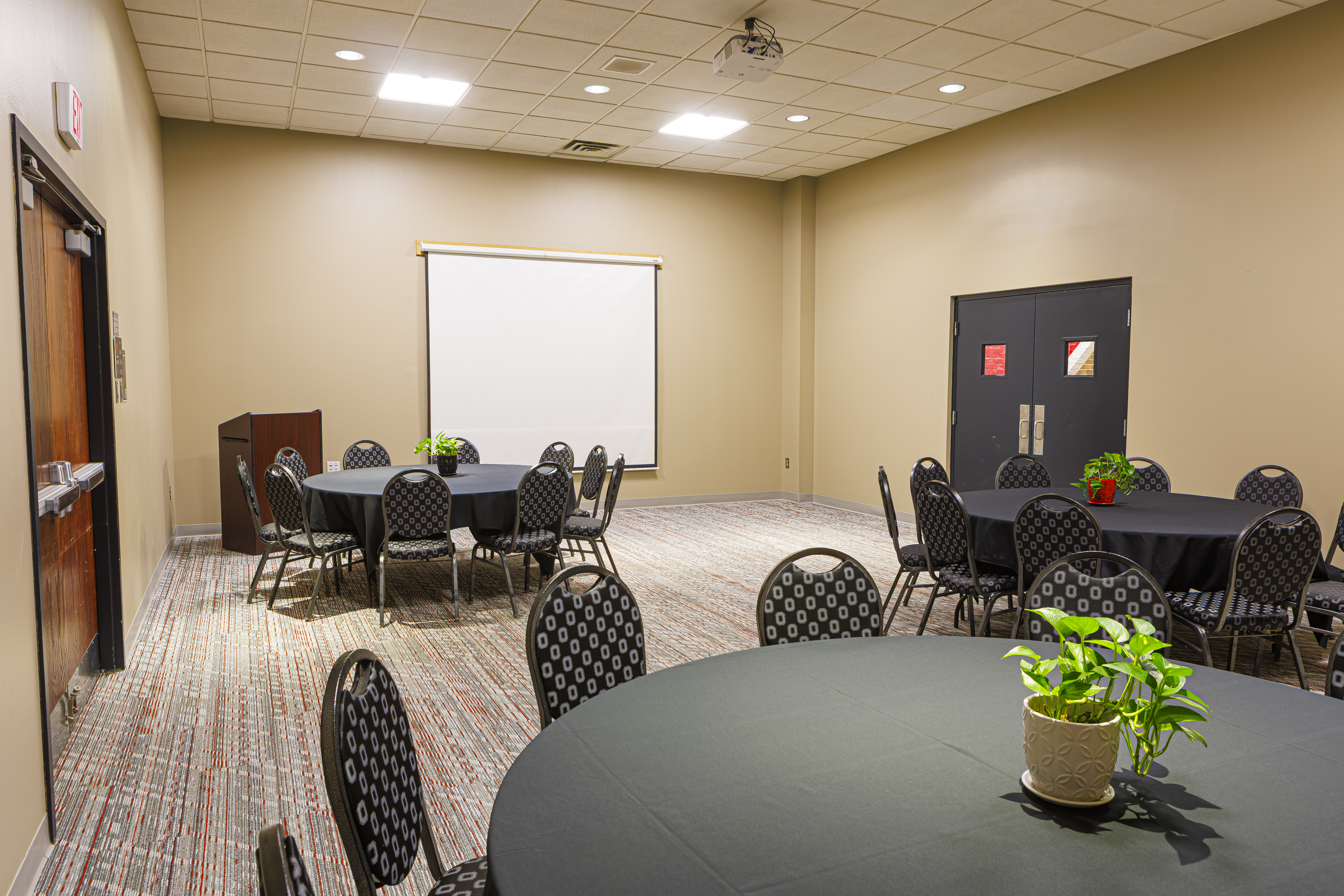 Meeting room with round tables, black linens, a projector screen, and a dark wood podium.