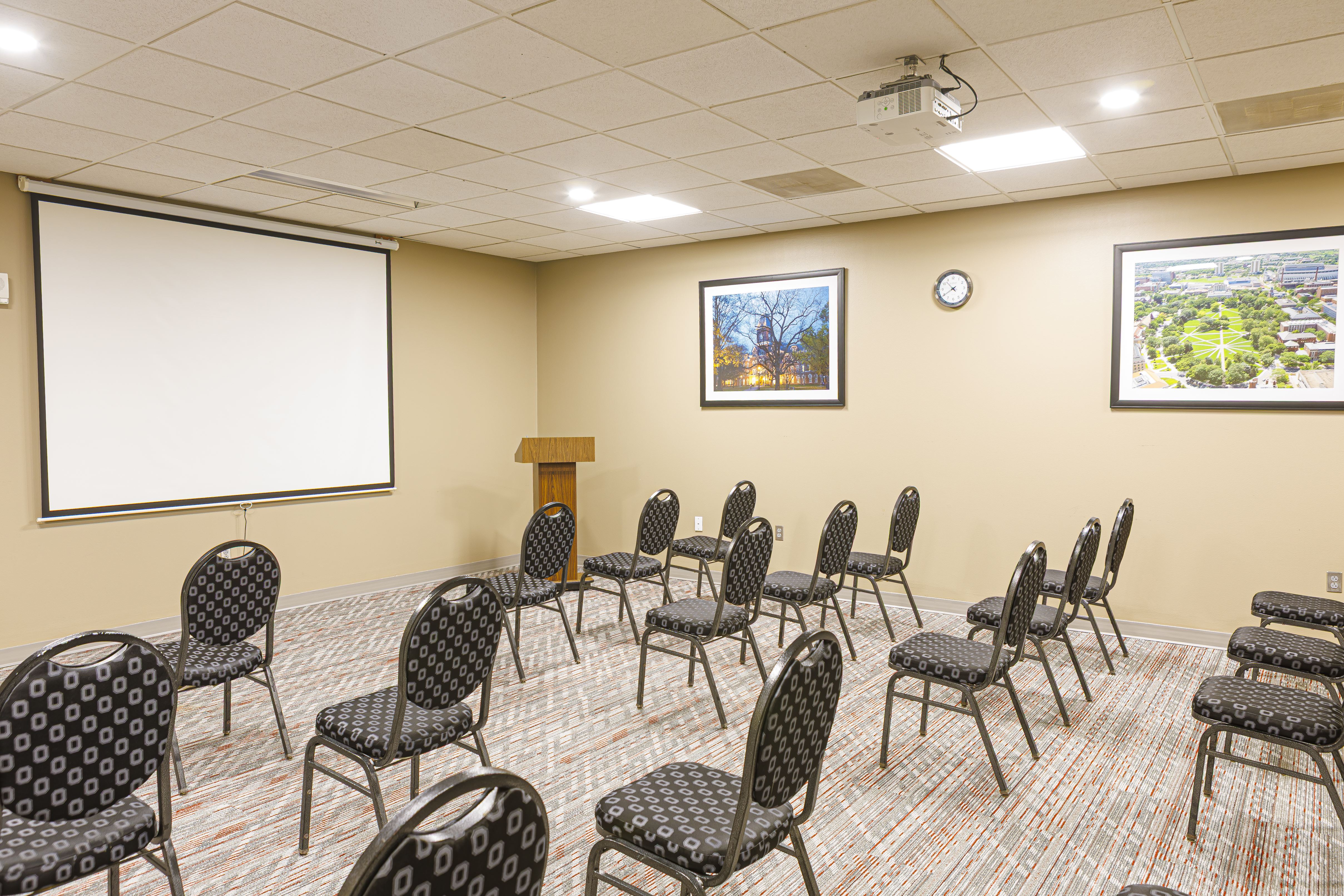 Small meeting room with rows of chairs facing a projector screen, wood podium, and two framed photos on the wall.